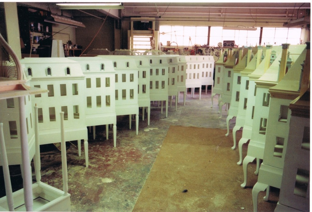 Dollhouses in production within workshop, about 25, all painted white. Lined up in two diagonal lines.