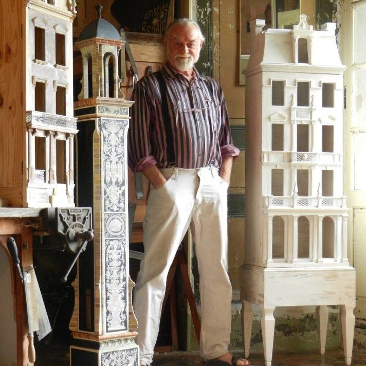 Eric in front of 3 magnificent dollhouses. One tower dollhouse with blue ornate decorations, one white chateau with delicate leaves, and the third a natural facade.