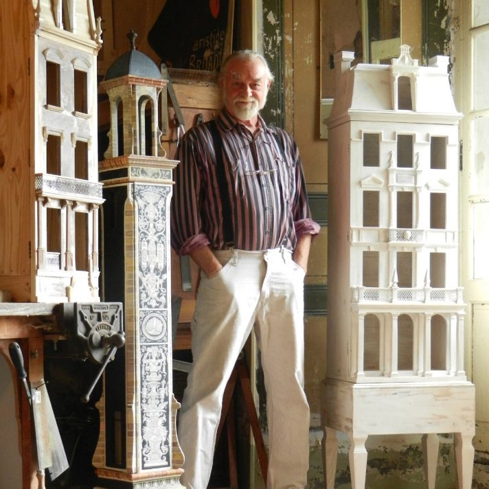 Eric in front of 3 magnificent dollhouses. One tower dollhouse with blue ornate decorations, one white chateau with delicate leaves, and the third a natural facade.