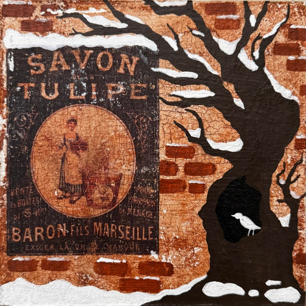 A barren winter tree twists in front of a red brick wall with an antique blue Savon Tulipe poster. Everything is dusted with snow.